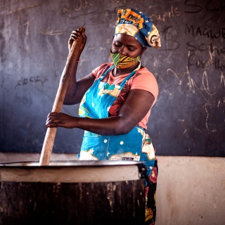 A volunteer cook prepares food in a cooking pot