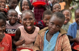 A group of school children posing with plates of food and looking into camera.