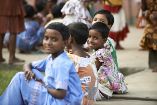 Image of children sitting on a step together with some of them turning to smile at the camera. 