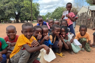 Image of children in Mozambique smiling and posing with their thumbs up to the camera. 